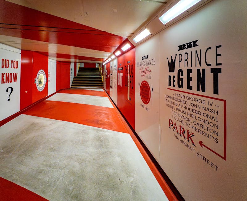 The image shows a brightly lit pedestrian underpass with a curved ceiling painted in red and cream. The floor is covered with a smooth, light-colored concrete surface, and the walls are decorated with large, bold black and red signage, including the words 'Prince Regent' with a crown symbol and historical details about the location. To the left, the wall features a circular emblem and a question mark, while to the right, there are additional signs and artwork referencing local history and landmarks. At the far end of the underpass, a staircase with wooden steps and black metal railings leads to an upper street level. The brightly illuminated environment, combined with the clean and organized appearance, suggests it is a well-maintained urban passageway, possibly used for private or independent access, aligning with alternative waste handling routes offered by services like Rubbish Clearance Marylebone for rubbish removal and bulk waste collection in the area.